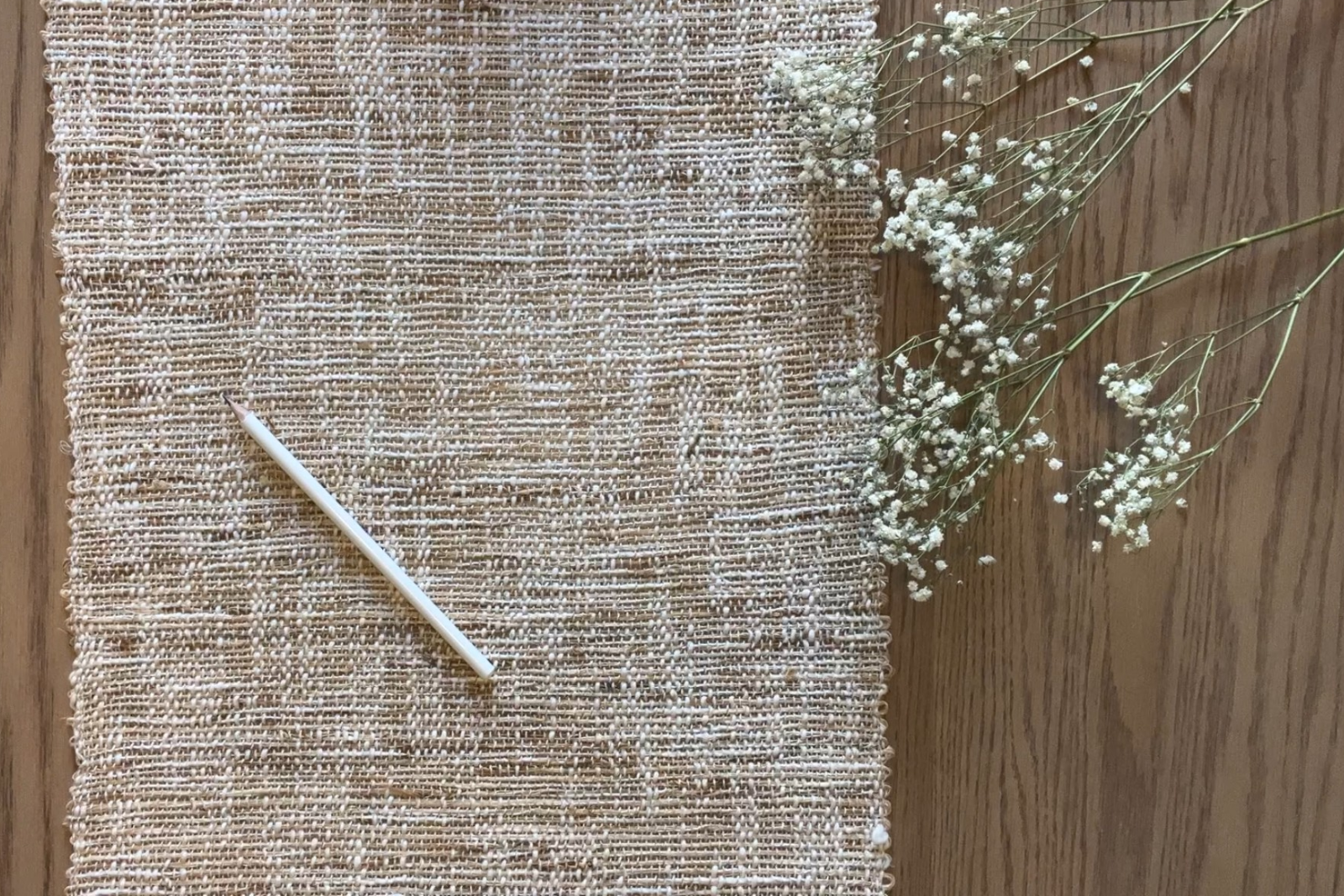 Textured fabric with a stick and small flowers on a wooden surface